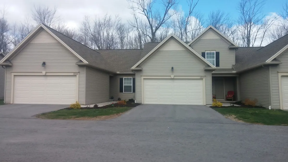 Mowed front lawn and driveway of a tan single-story home in Webster, NY