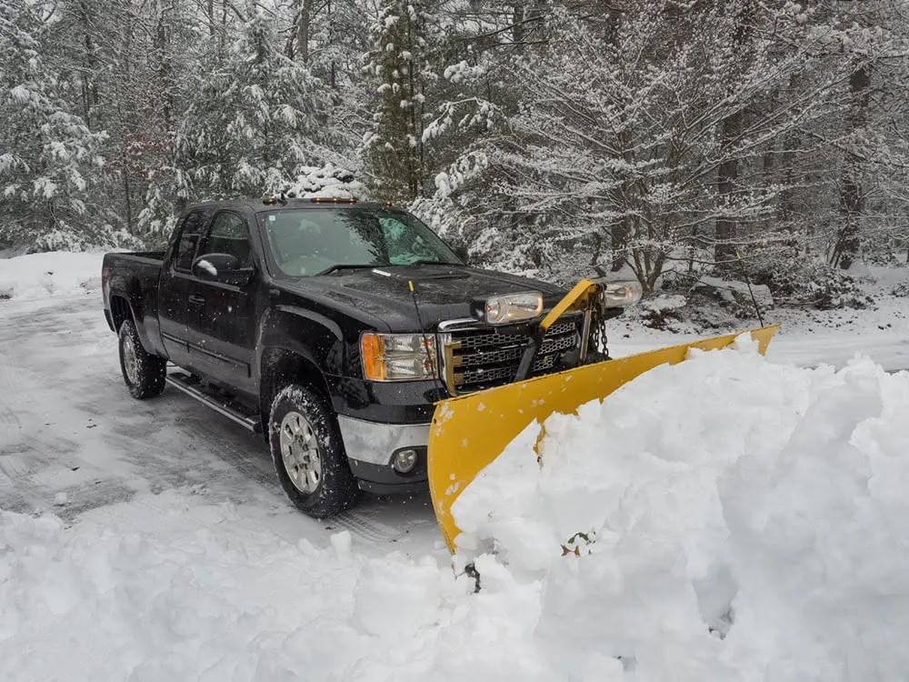 Black GMC pickup with a yellow snow plow parked in a plowed driveway