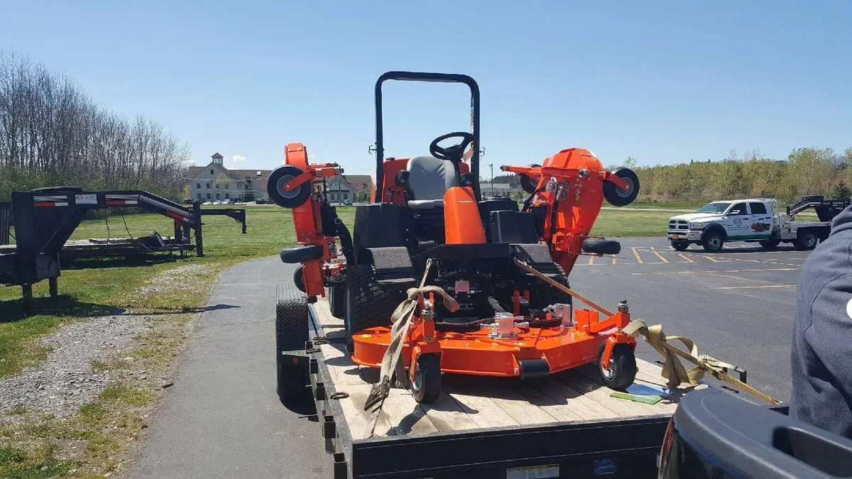Matt's orange commercial mower strapped down on a trailer behind the truck