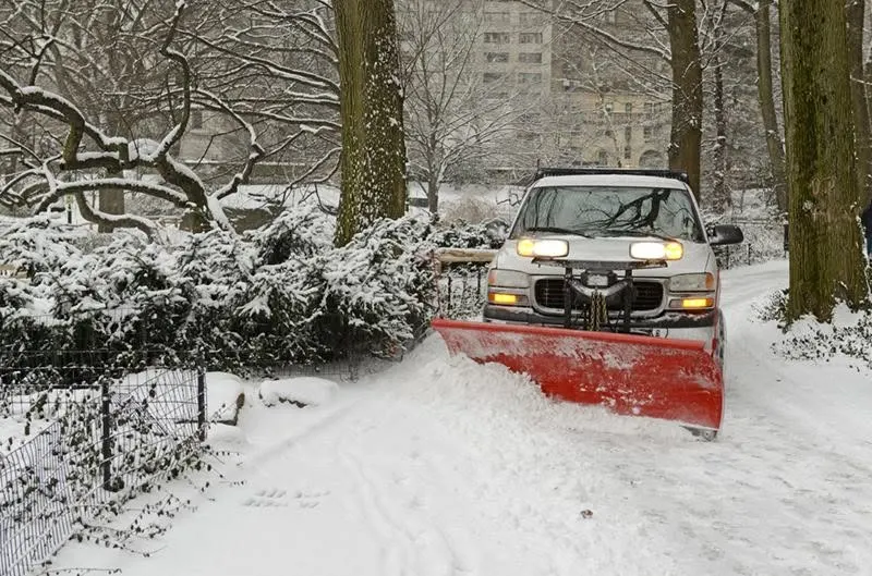 Pickup with a red plow clearing a driveway under snow-covered trees after a storm in Webster, NY